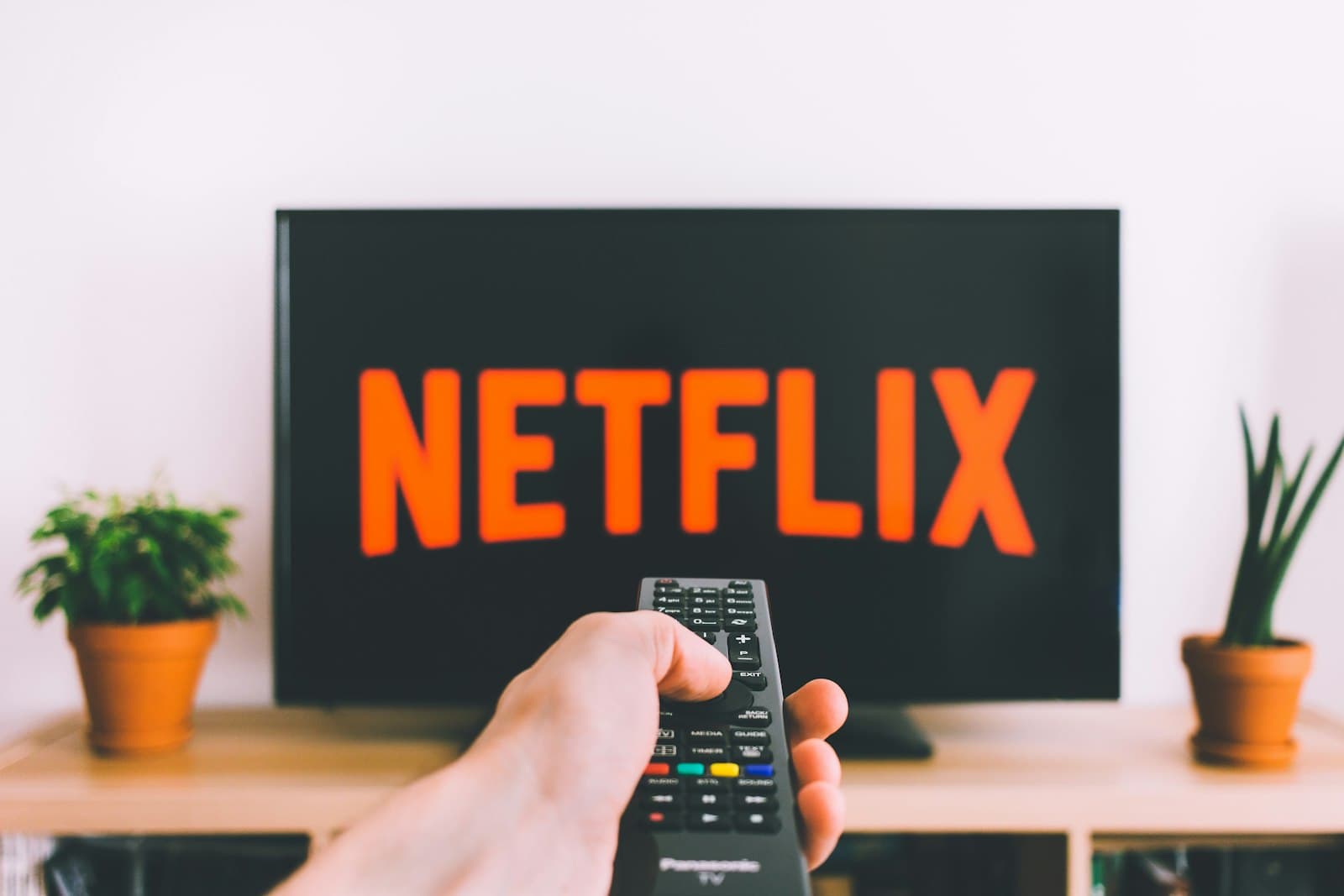 A hand pointing a TV remote at a streaming screen